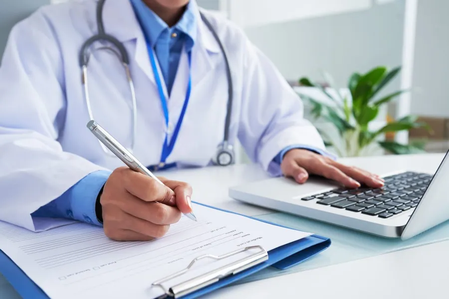 Médica em consultório anotando o prontuário do paciente